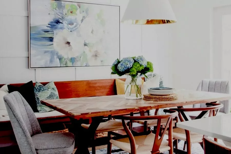 Inside farmhouse room, Colorful flower painting hang on wall. In center of the room table is set and around it sofa & chair